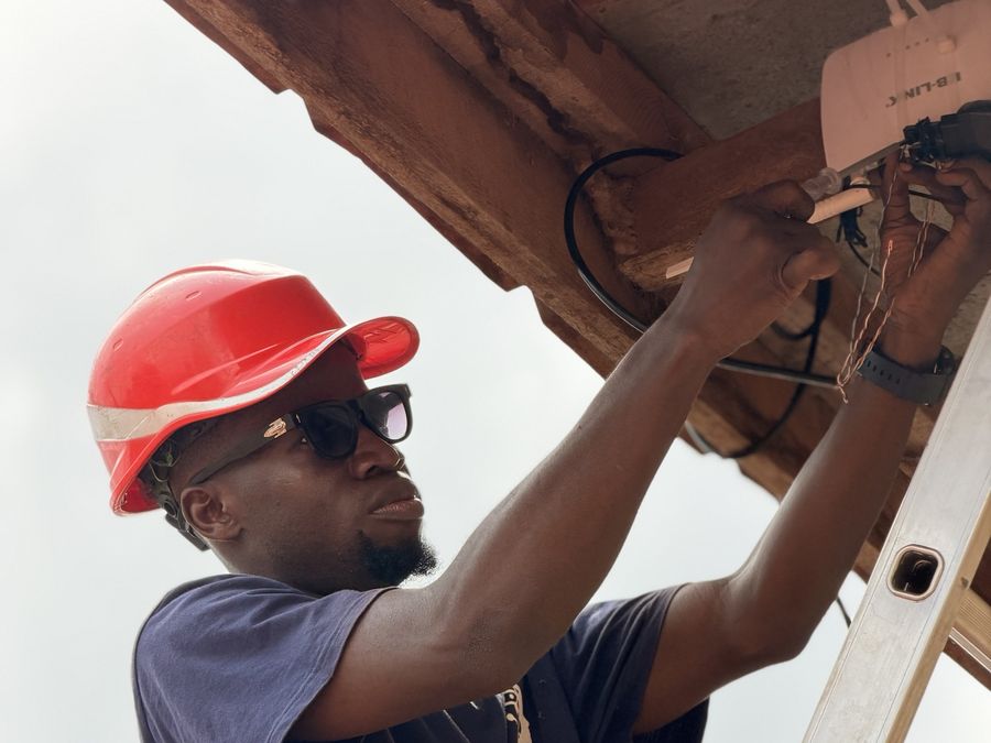 Technicien MBS installant un équipement réseau sous un toit, sur une échelle